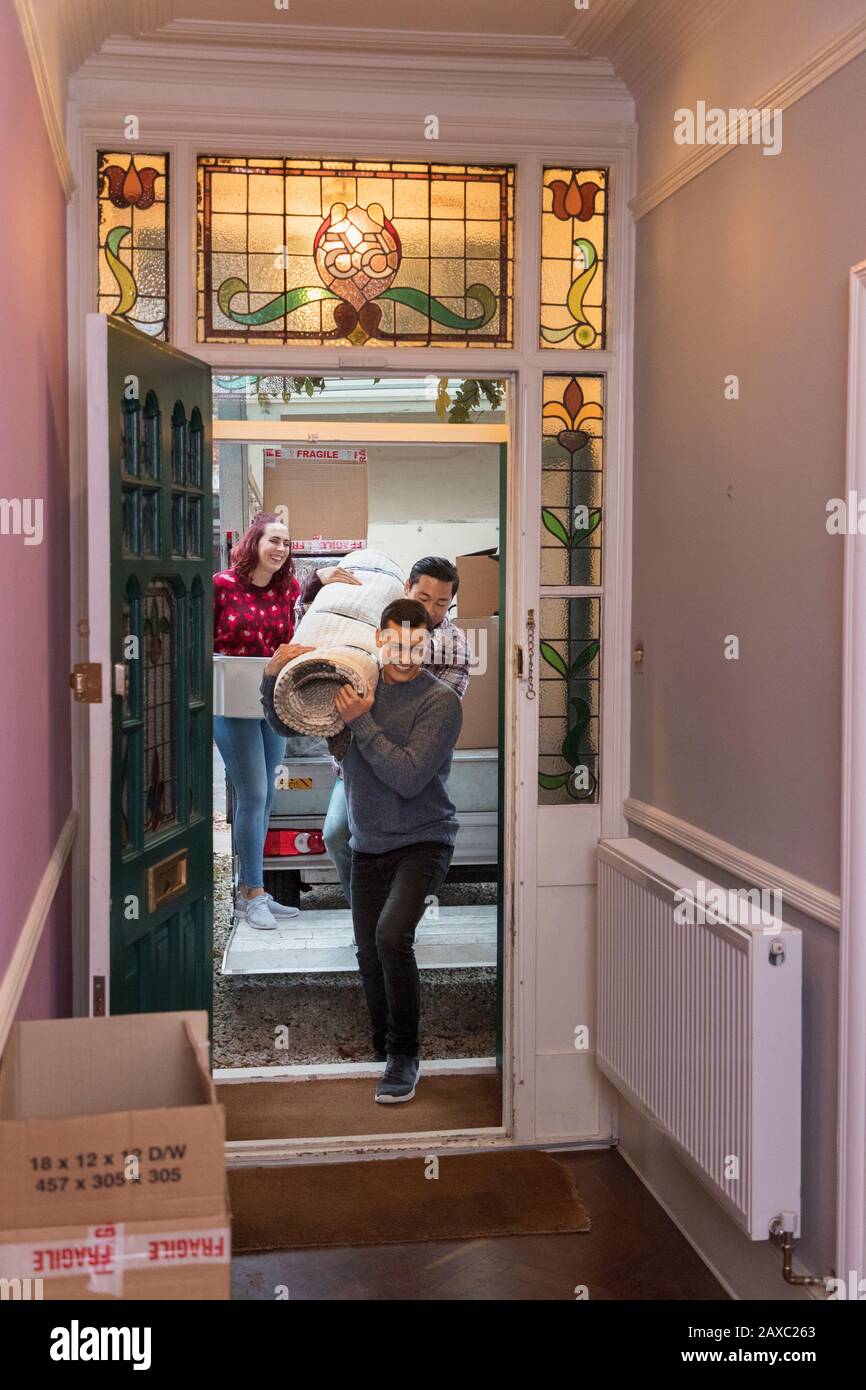 Freunde ziehen Haus, tragen Teppich durch die Haustür Stockfoto