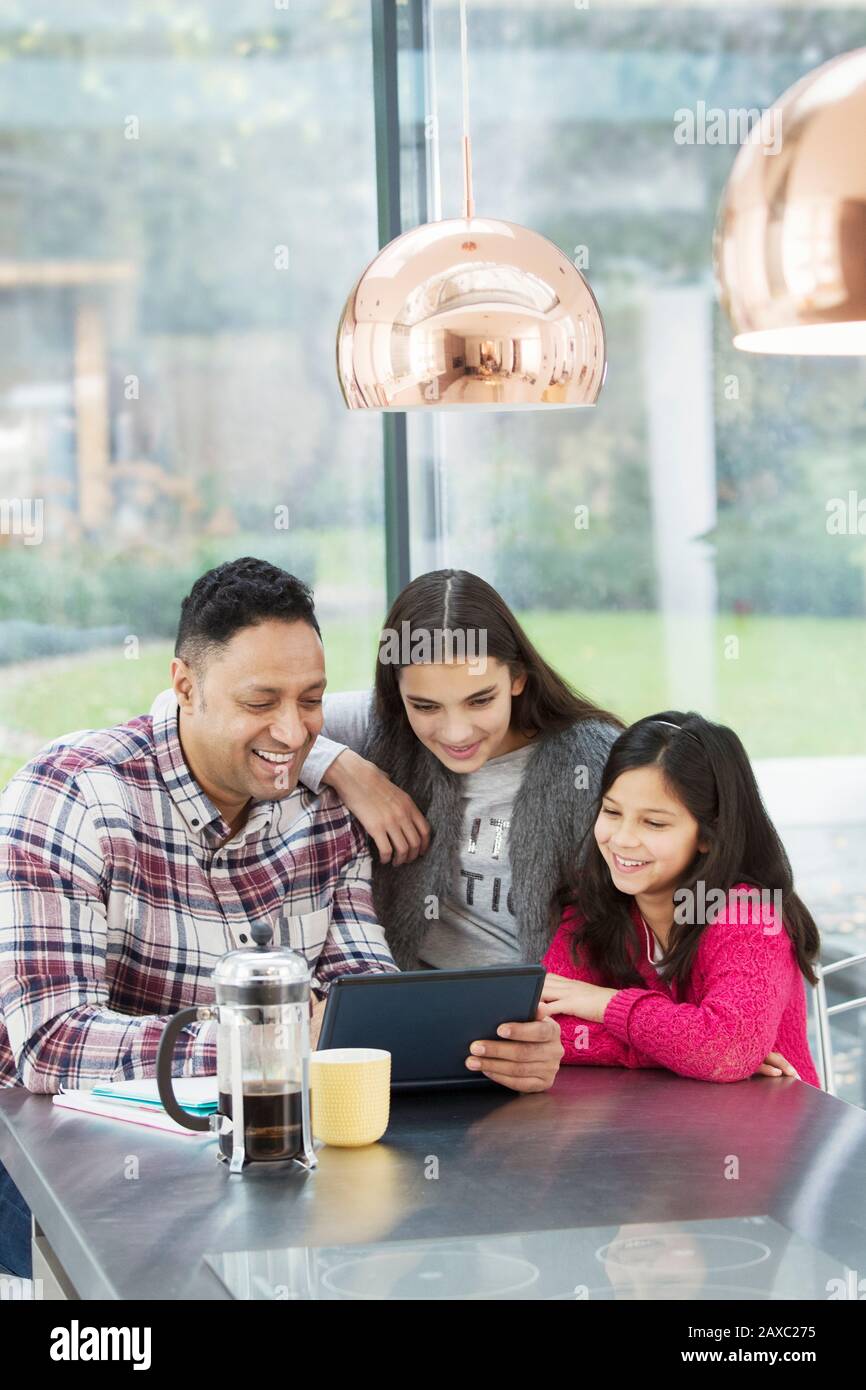 Glücklicher Vater und Töchter, die ein digitales Tablett in der Morgenküche verwenden Stockfoto