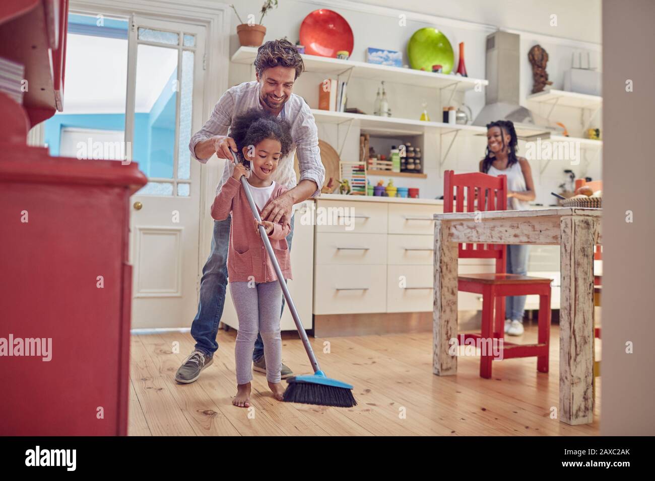 Vater und Tochter fegen Küchenboden mit Besen Stockfoto