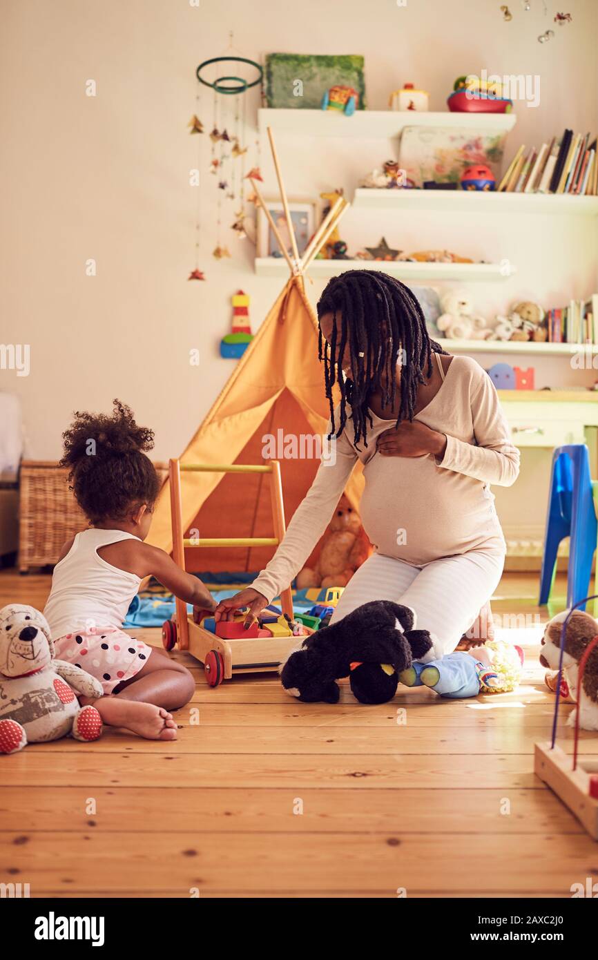 Schwangere Mutter und kleine Tochter, die mit Spielzeug spielen Stockfoto