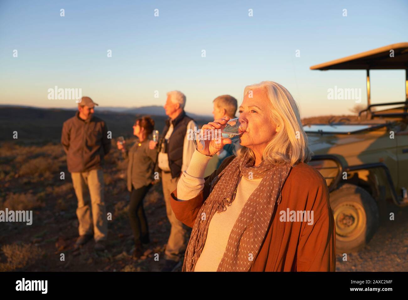 Seniorin auf Safari, die Champagner bei Sonnenuntergang trinkt Stockfoto