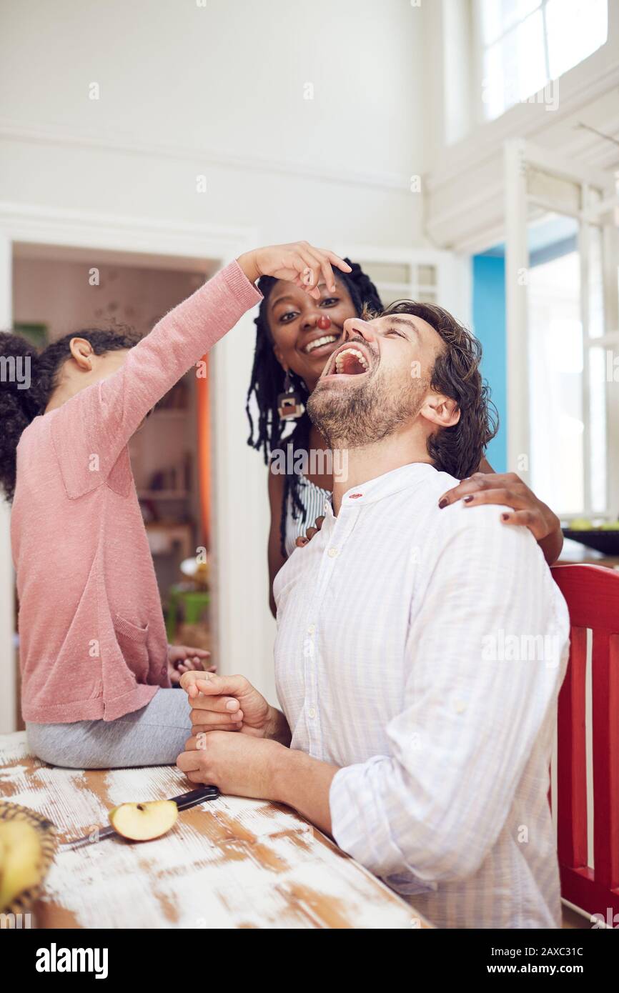 Verspielte Tochter füttert Vater Traube am Küchentisch Stockfoto