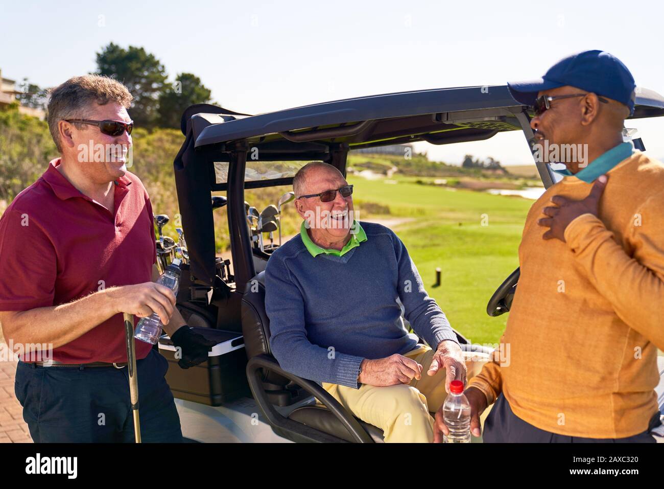 Männliche Freunde, die auf dem sonnigen Golfplatz in der Golfkarre sprechen Stockfoto