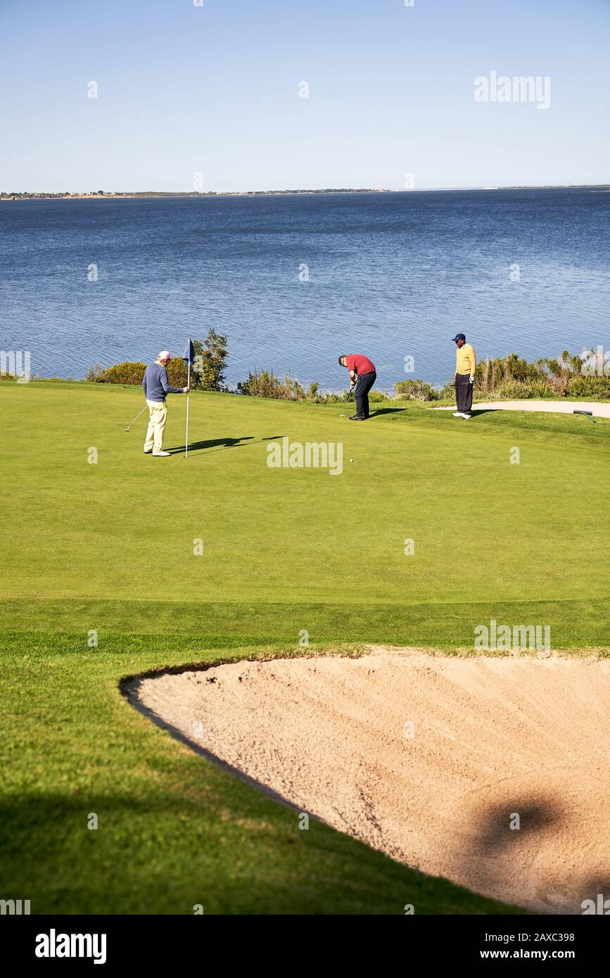 Männliche Golfer am sonnigen Seeufer, der grün wird Stockfoto