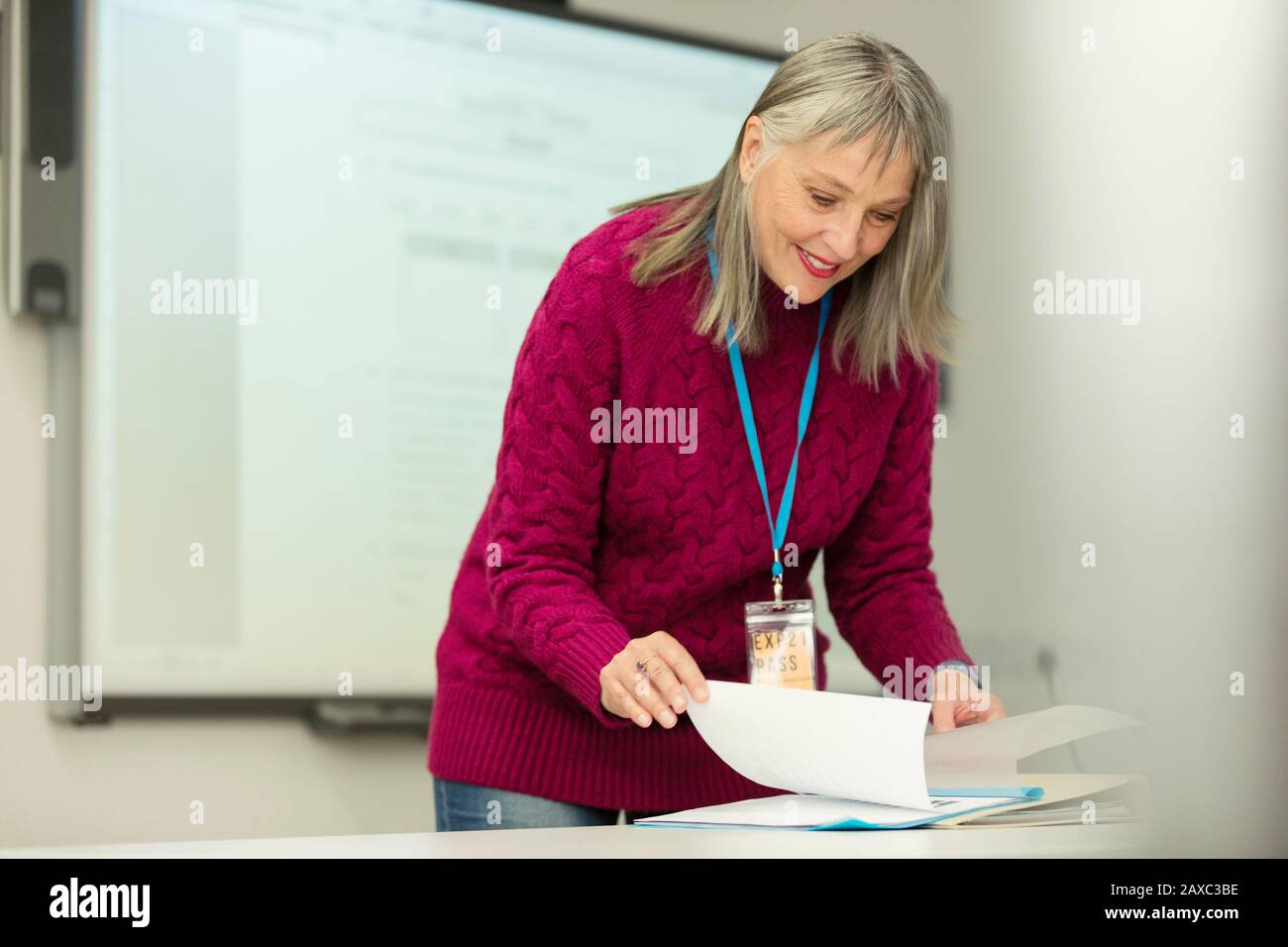 Lächelnde Dozentin mit Schreibarbeit im Klassenzimmer Stockfoto