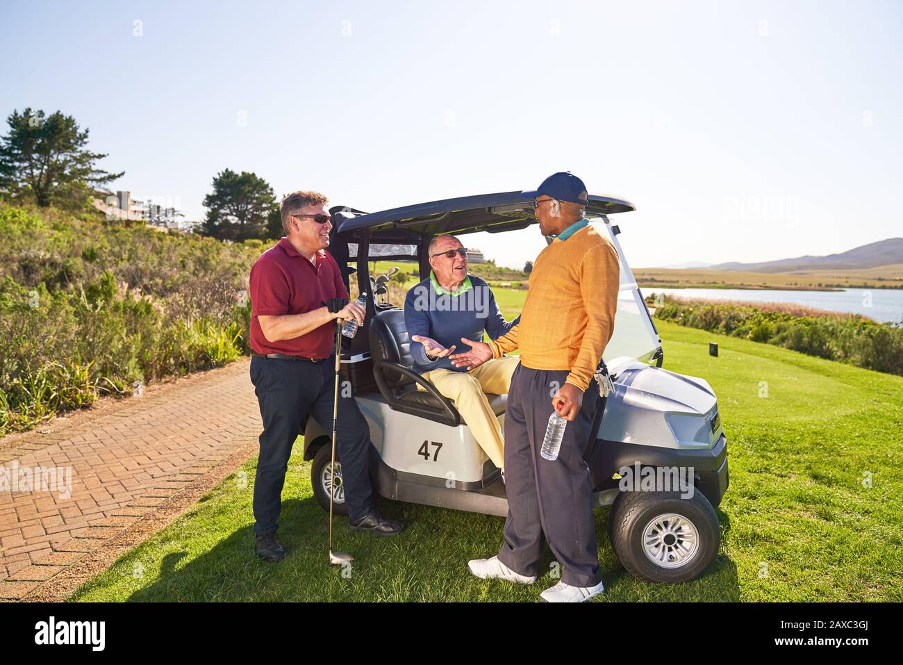 Männliche Golfspielerfreunde, die auf der sonnigen Golfkarre sprechen Stockfoto