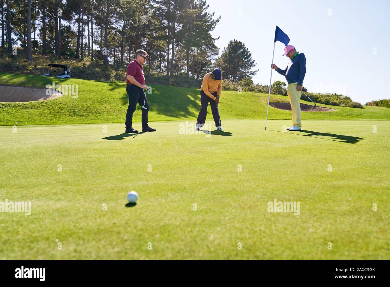 Männliche Golfspielerfreunde, die zu Hause auf einem sonnigen Golfplatz spielen Stockfoto