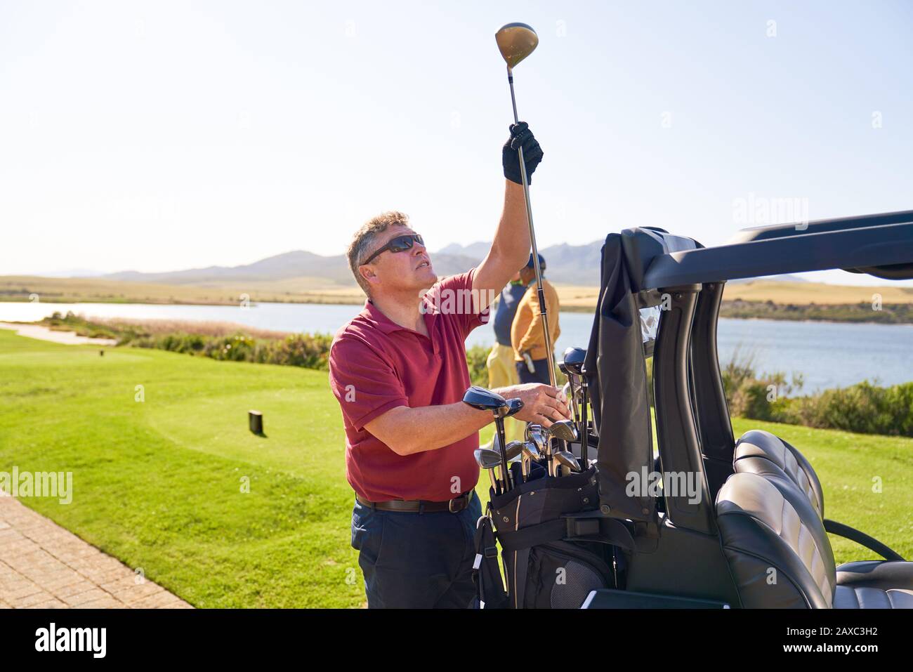 Golfer, der sich für einen Golfclub im T-Shirt Box auf einem sonnigen Golfplatz entscheidet Stockfoto