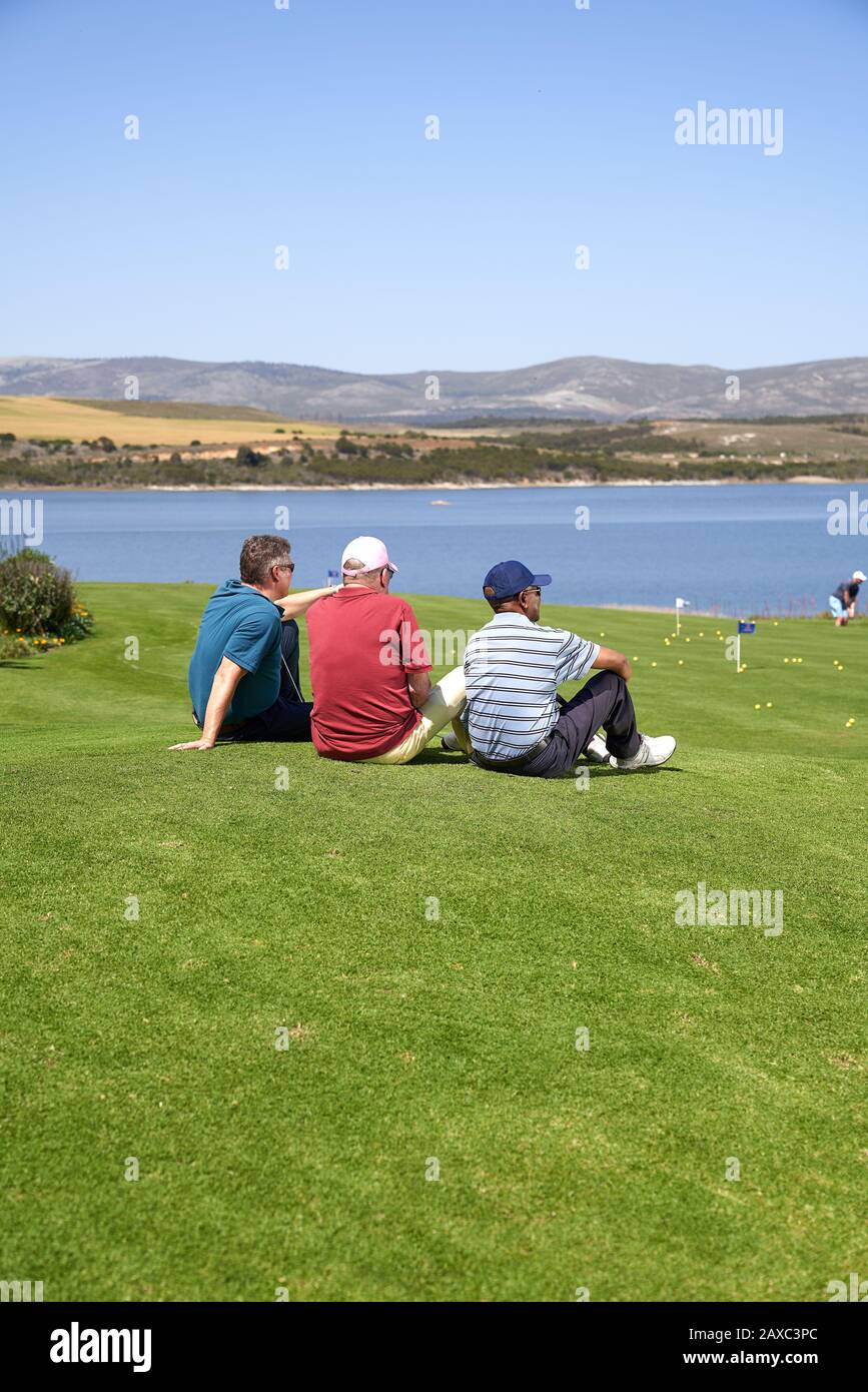 Männliche Golfer, die auf einem sonnigen Golfplatz eine Pause im Gras machen Stockfoto