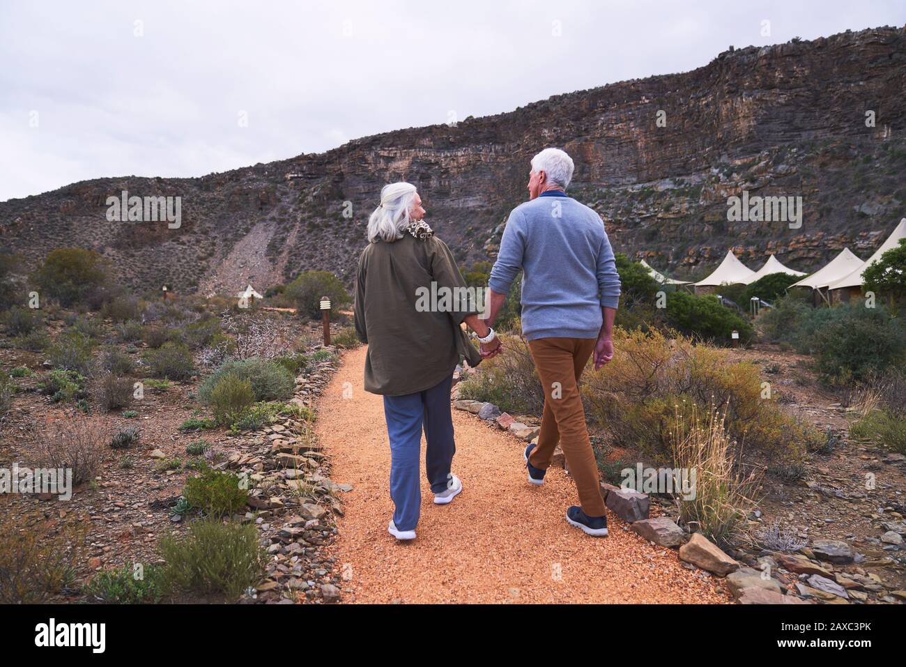 Älteres Paar hält die Hände auf dem Fußweg vor den Safari-Lodge-Kabinen Stockfoto