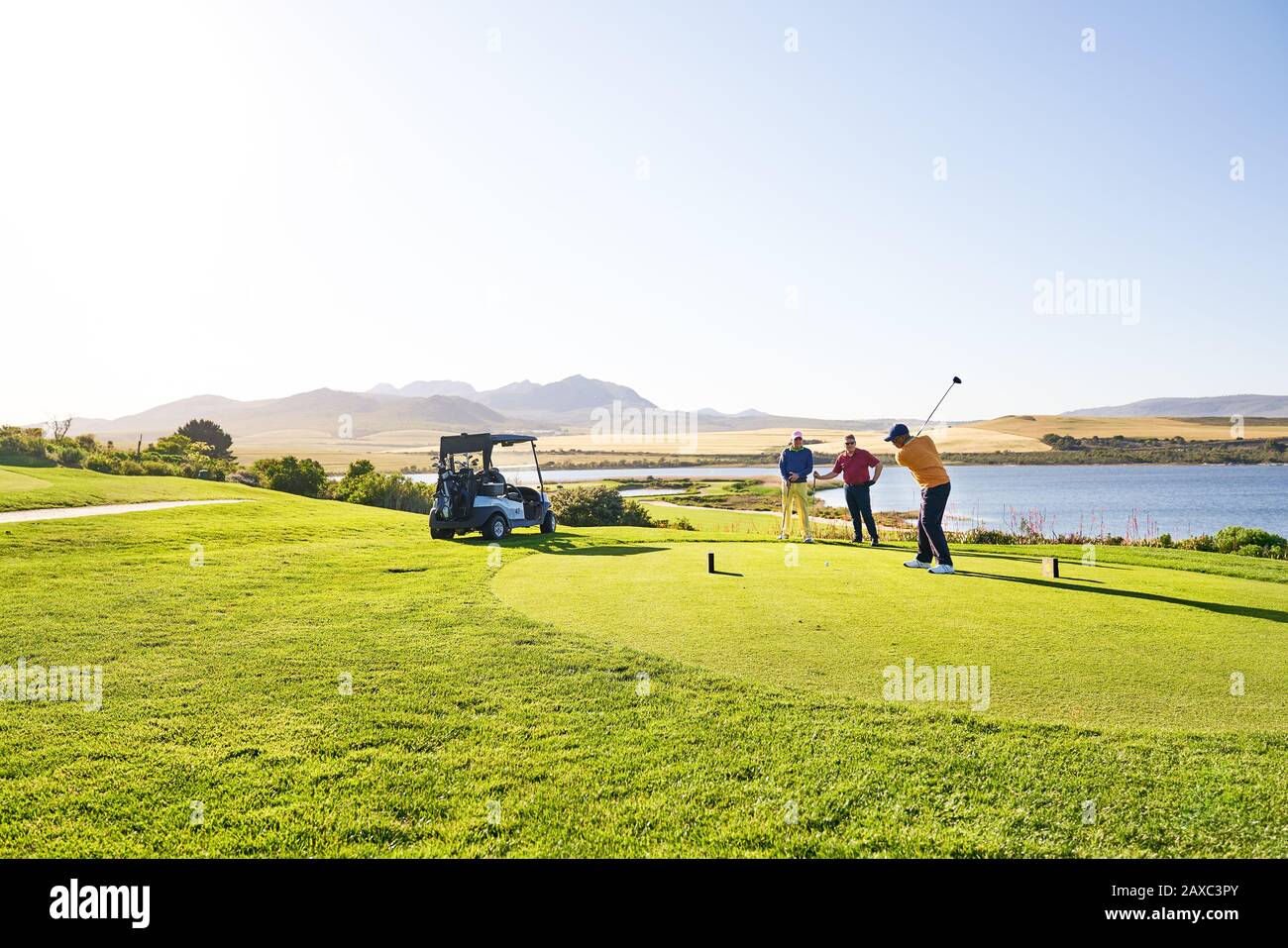 Männlicher Golfer, der an der sonnigen T-Box-Box am See abzweigte Stockfoto