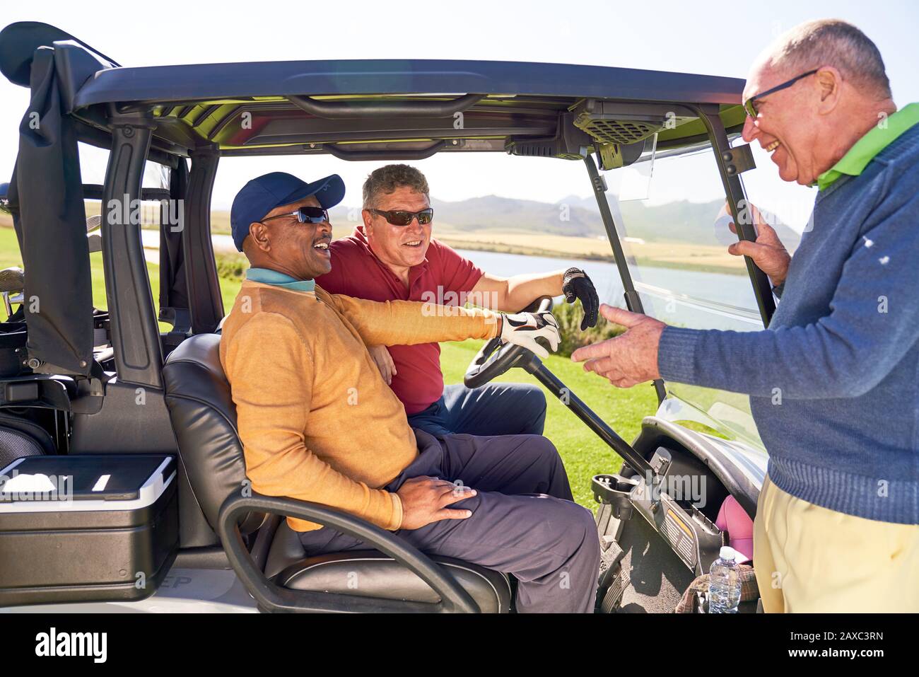 Männliche Golfer, die auf der sonnigen Golfkarre sprechen Stockfoto