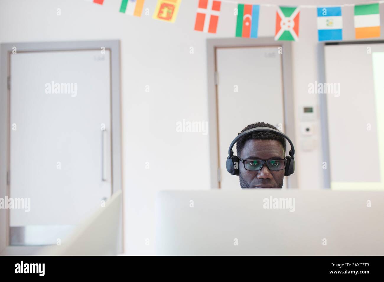Student der männlichen Community mit Kopfhörern am Computer im Klassenzimmer Stockfoto