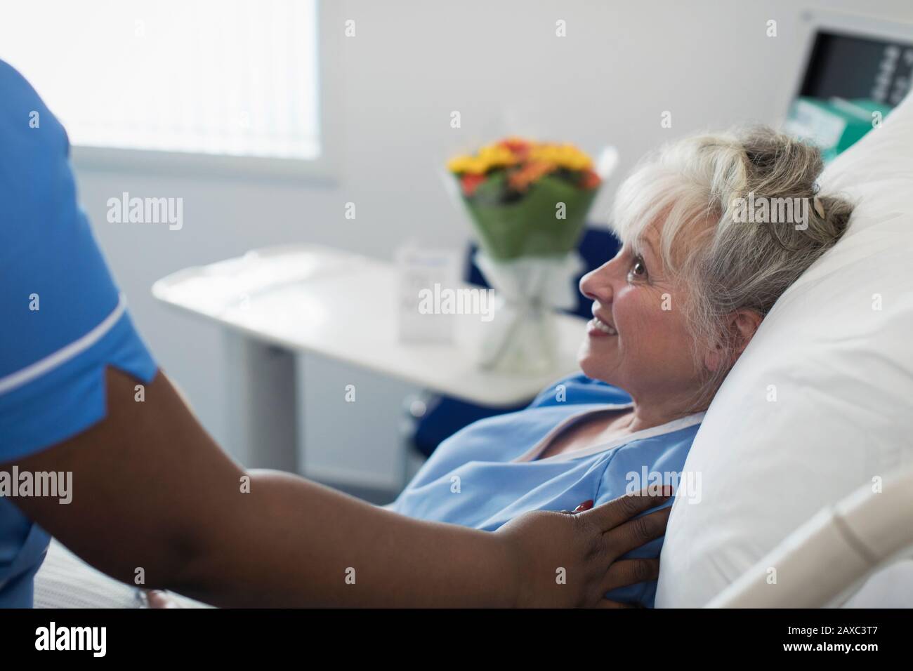 Pflegende weibliche Krankenschwester tröstet die ältere Frau, die im Krankenbett ruht Stockfoto