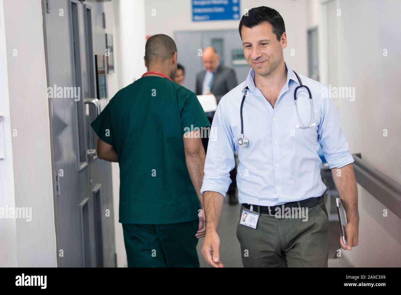 Männlicher Arzt mit digitaler Tablette, der im Krankenhausflur spazieren geht Stockfoto