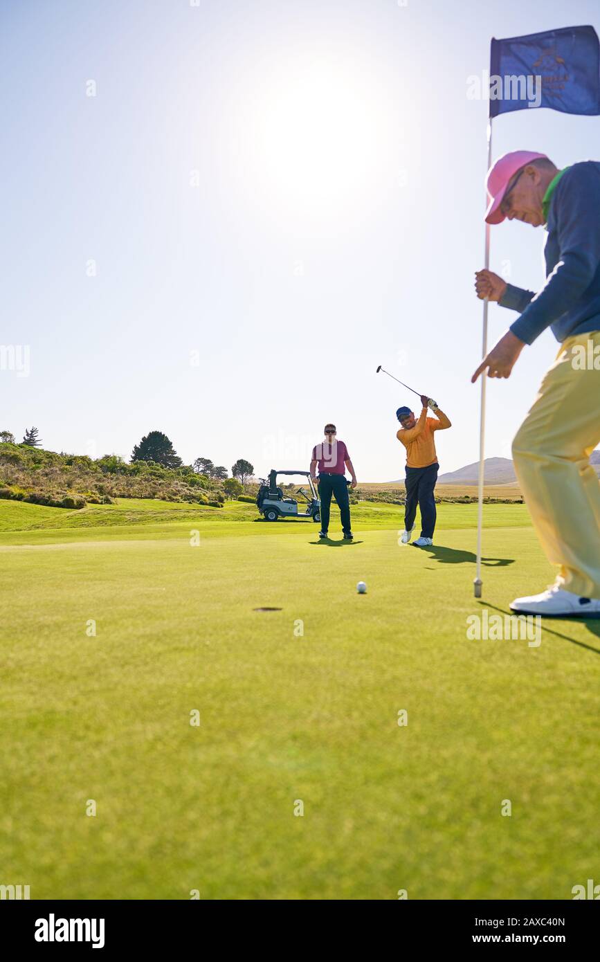 Männlicher Golfer, der auf dem sonnigen Golfplatz in Richtung Loch legt, der grün wird Stockfoto