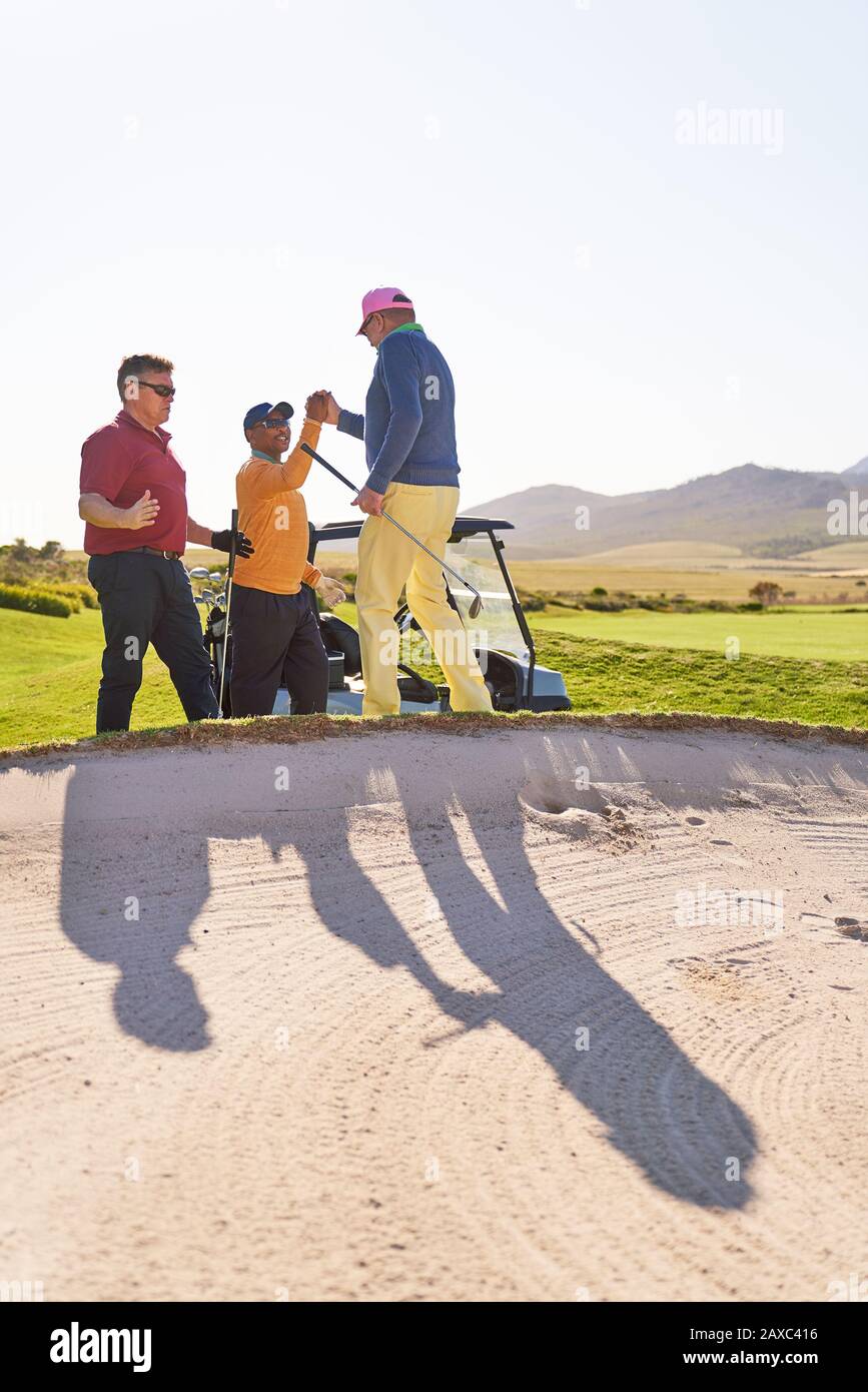 Männliche Golfer feiern hinter sonnigen Golfbunkern Stockfoto