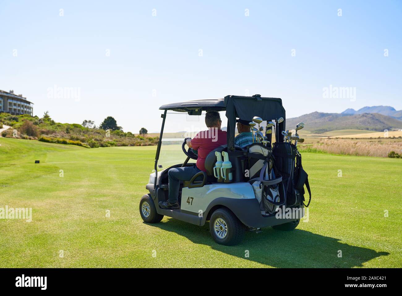 Männliche Golfer, die Golfwagen auf sonnigen Golfplätzen fahren Stockfoto