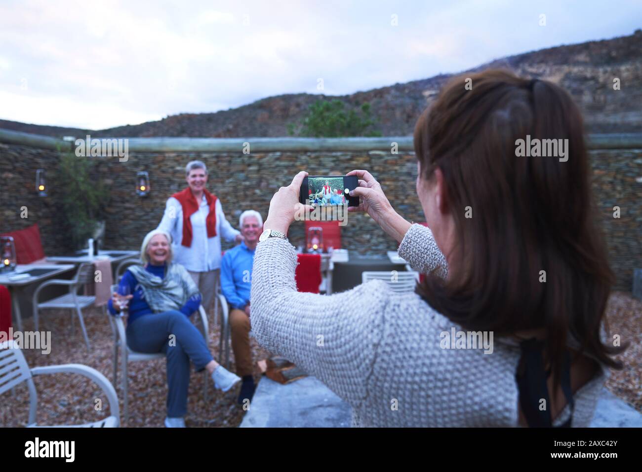 Frau mit Kameratelefon fotografiert ältere Freunde auf der Hotelterrasse Stockfoto