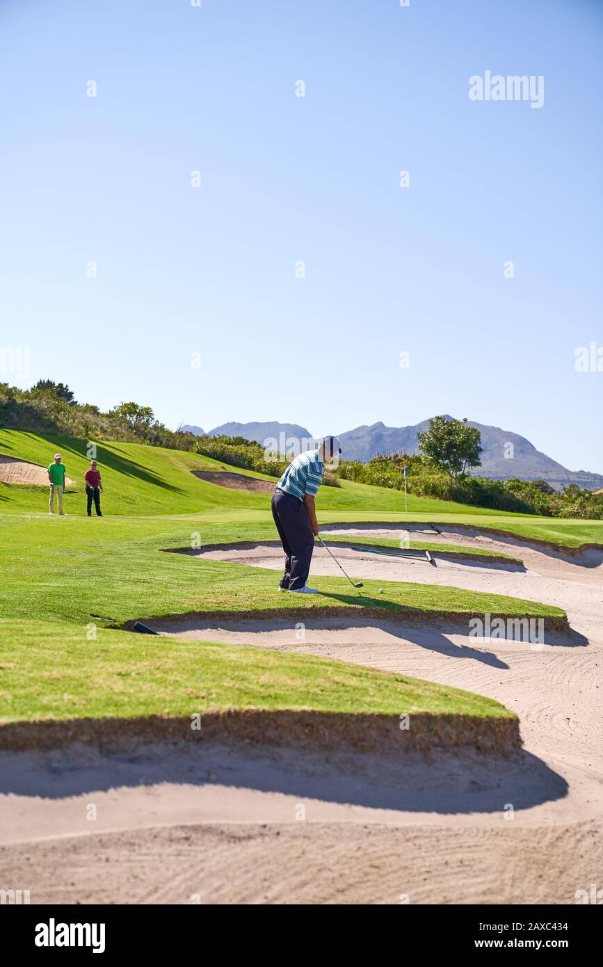 Männlicher Golfer, der sich vorbereitet, einen Schuss über dem sonnigen Golfplätzen Bunker zu machen Stockfoto