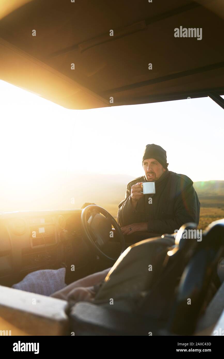 Safari-Tour-Guide trinkt Tee im Geländewagen bei Sonnenaufgang Stockfoto