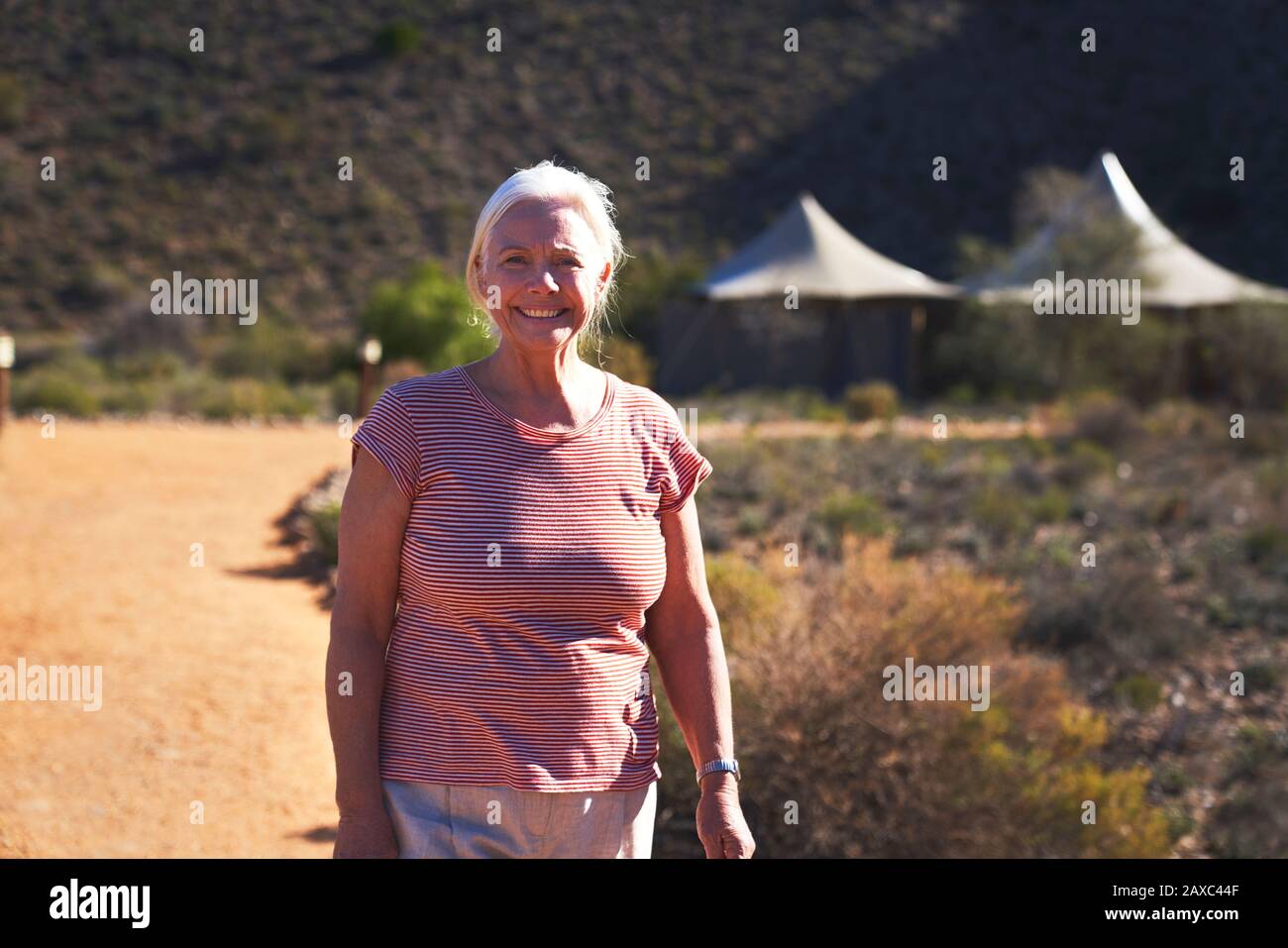 Portrait fröhliche ältere Frau auf sonnigen Fußweg vor der Safarihütte Stockfoto