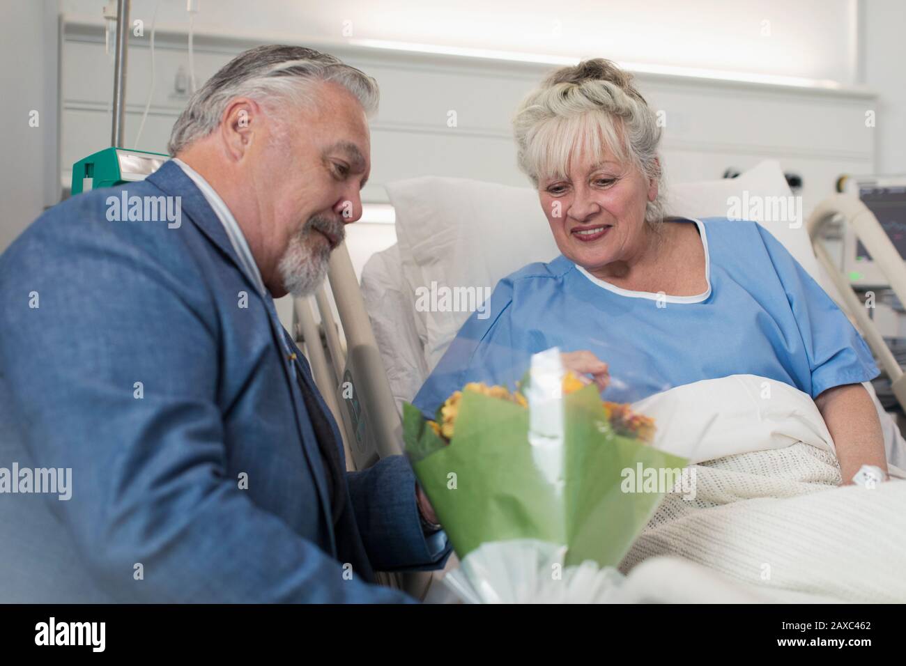 Älterer Mann bringt Blumenstrauß zur Frau, die im Krankenbett ruht Stockfoto