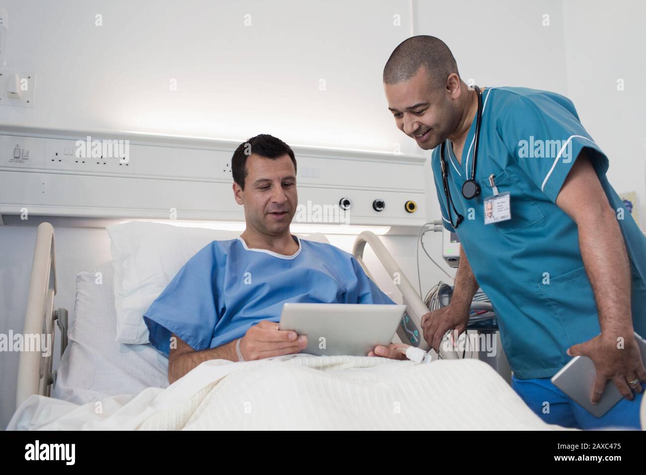 Männlicher Patient mit digitaler Tablette, der mit der Krankenschwester im Krankenhauszimmer spricht Stockfoto