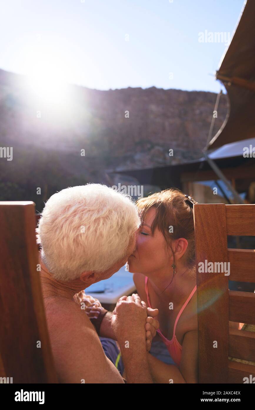 Fröhliches romantisches Senioren-Paar küsst auf sonnigen Balkon Stockfoto