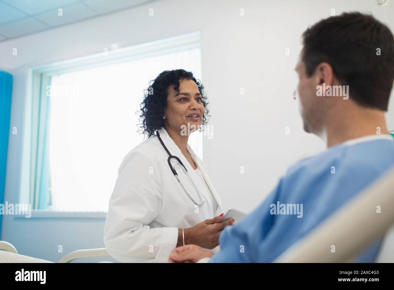 Arzt macht Runden und spricht mit dem Patienten im Krankenhauszimmer Stockfoto