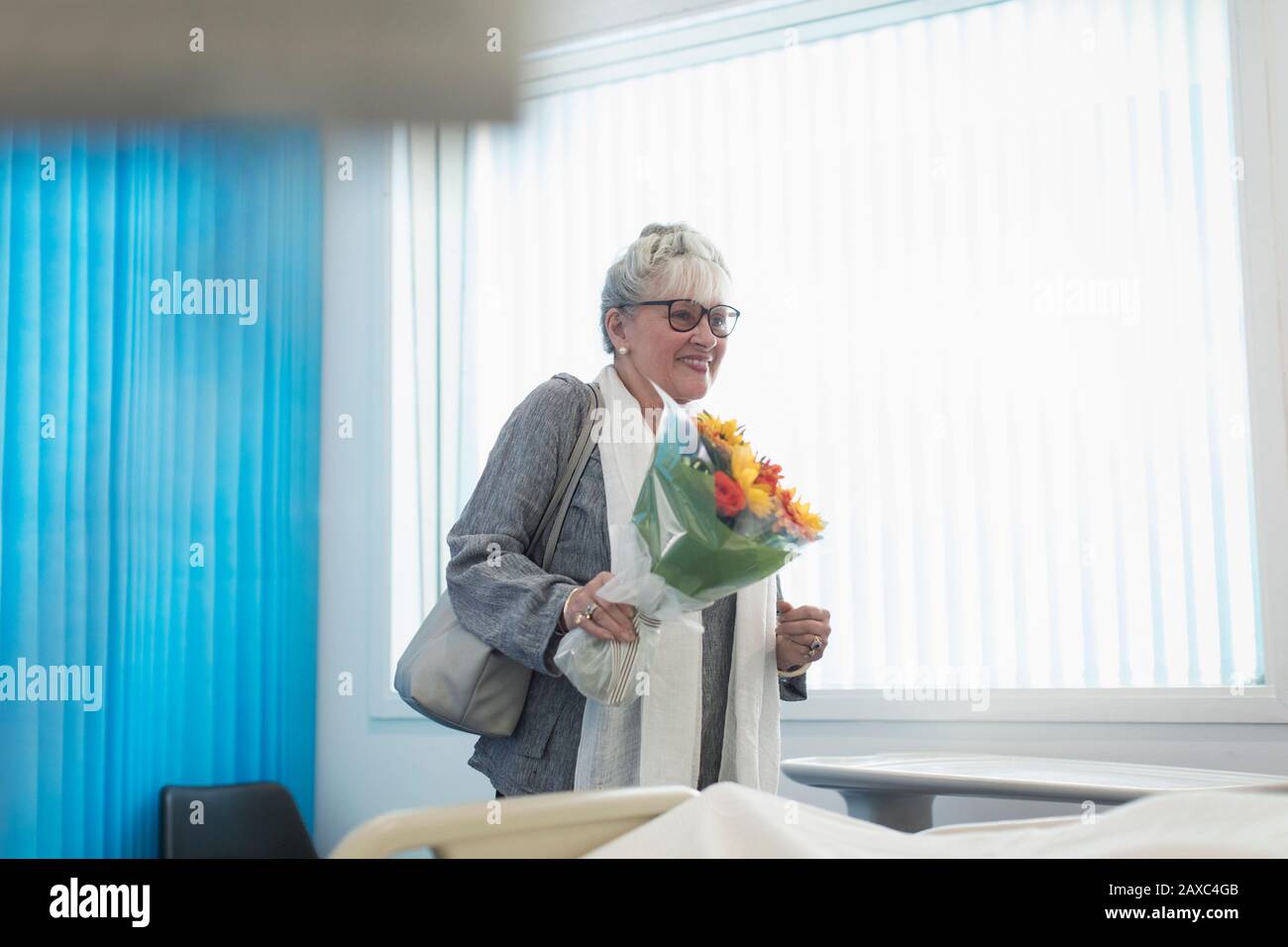 Lächelnde Senioren-Besucherin mit Blumenstrauß im Krankenzimmer Stockfoto