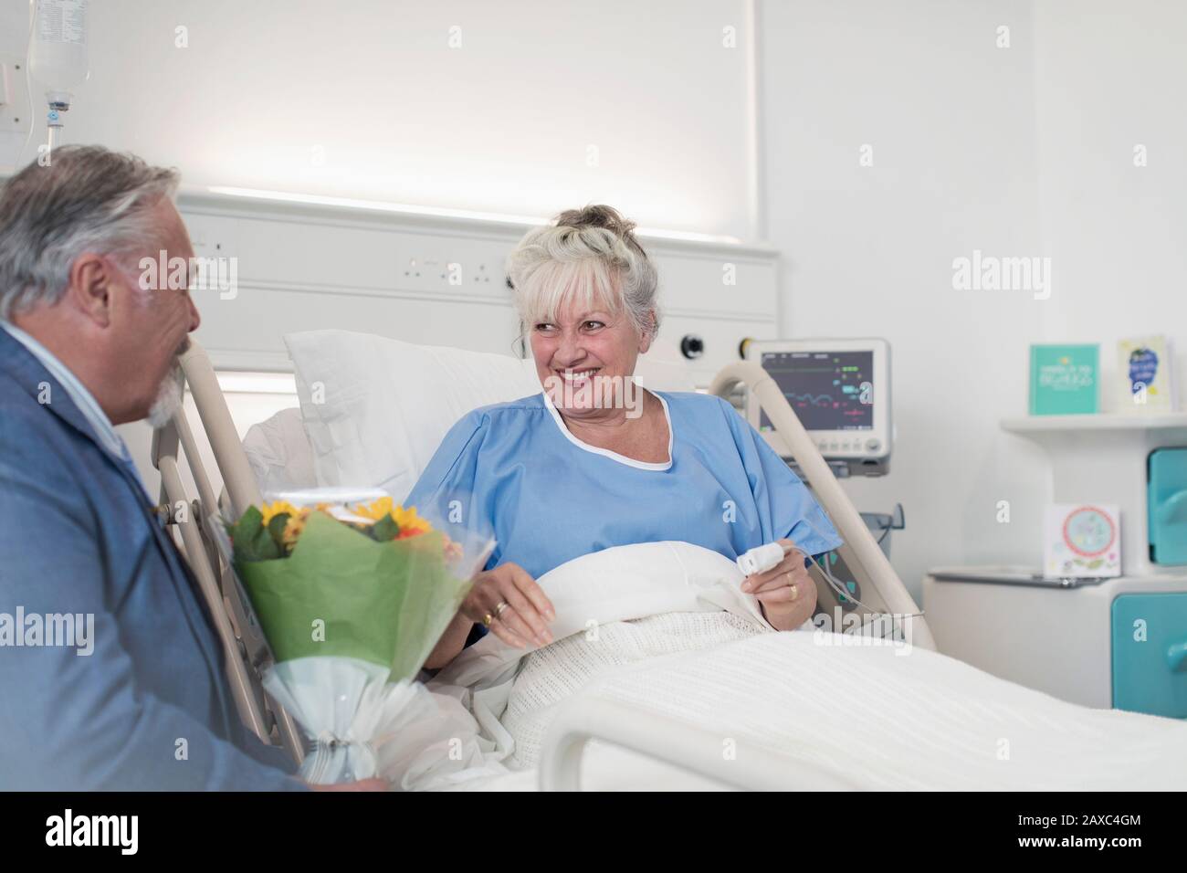 Leitender Mann mit Blumenstrauß, der Ehefrau im Krankenhaus besucht Stockfoto