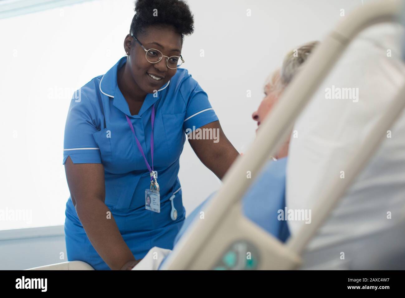 Lächelnde, fürsorgliche Krankenschwester, die mit dem Patienten im Krankenbett spricht Stockfoto
