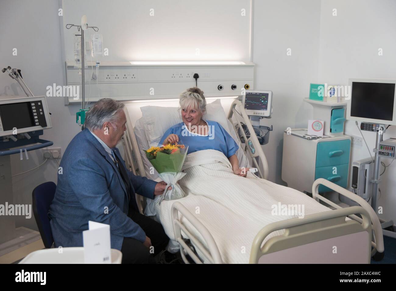 Leitender Mann mit Blumenstrauß, der die Frau besucht, die im Krankenzimmer ruht Stockfoto