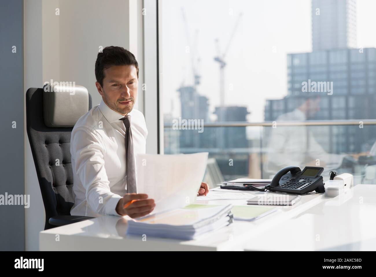 Unternehmer lesen Papierkram im sonnigen, städtischen Büro Stockfoto