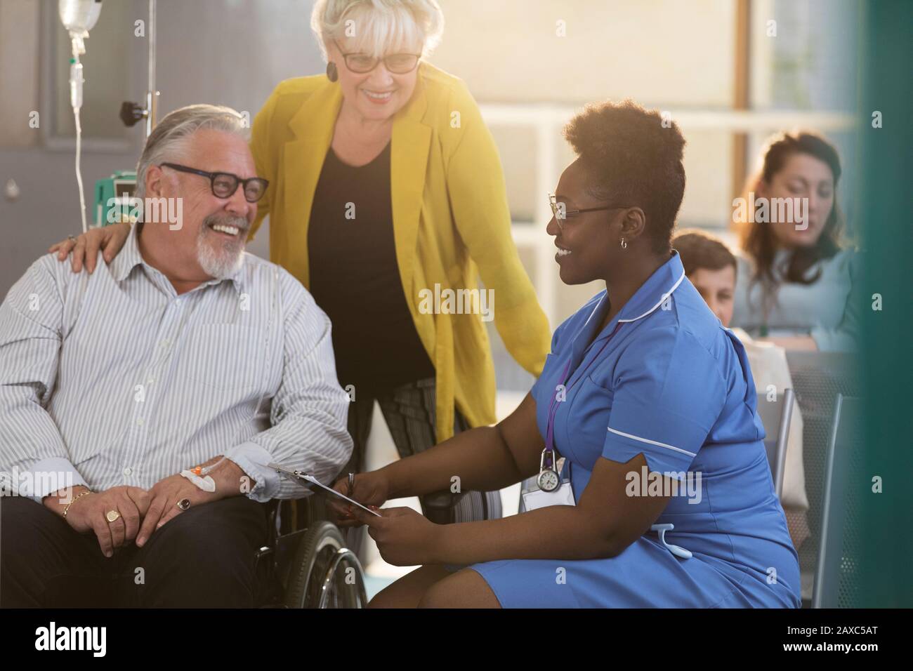 Weibliche Krankenschwester im Rollstuhl im Gespräch mit einer männlichen Senior-Patientin in der Lobby der Klinik Stockfoto