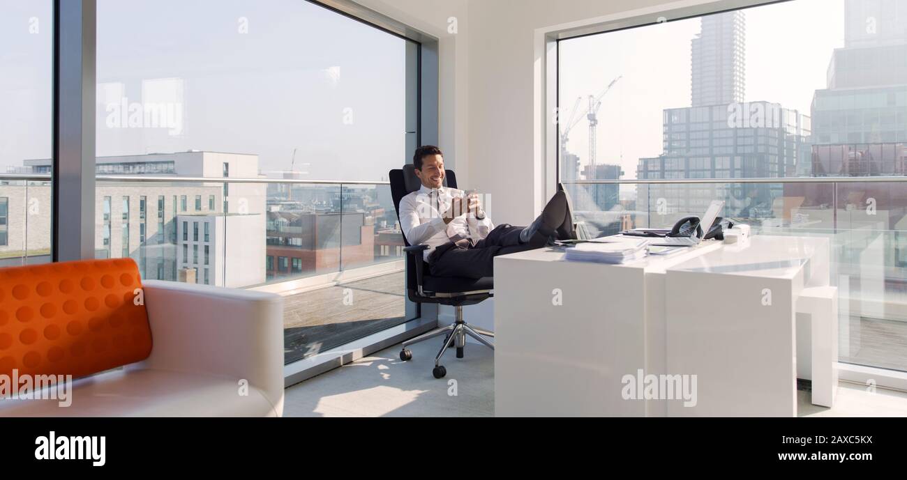 Geschäftsmann mit Füßen auf dem Schreibtisch in einem sonnigen, modernen, städtischen Büro Stockfoto