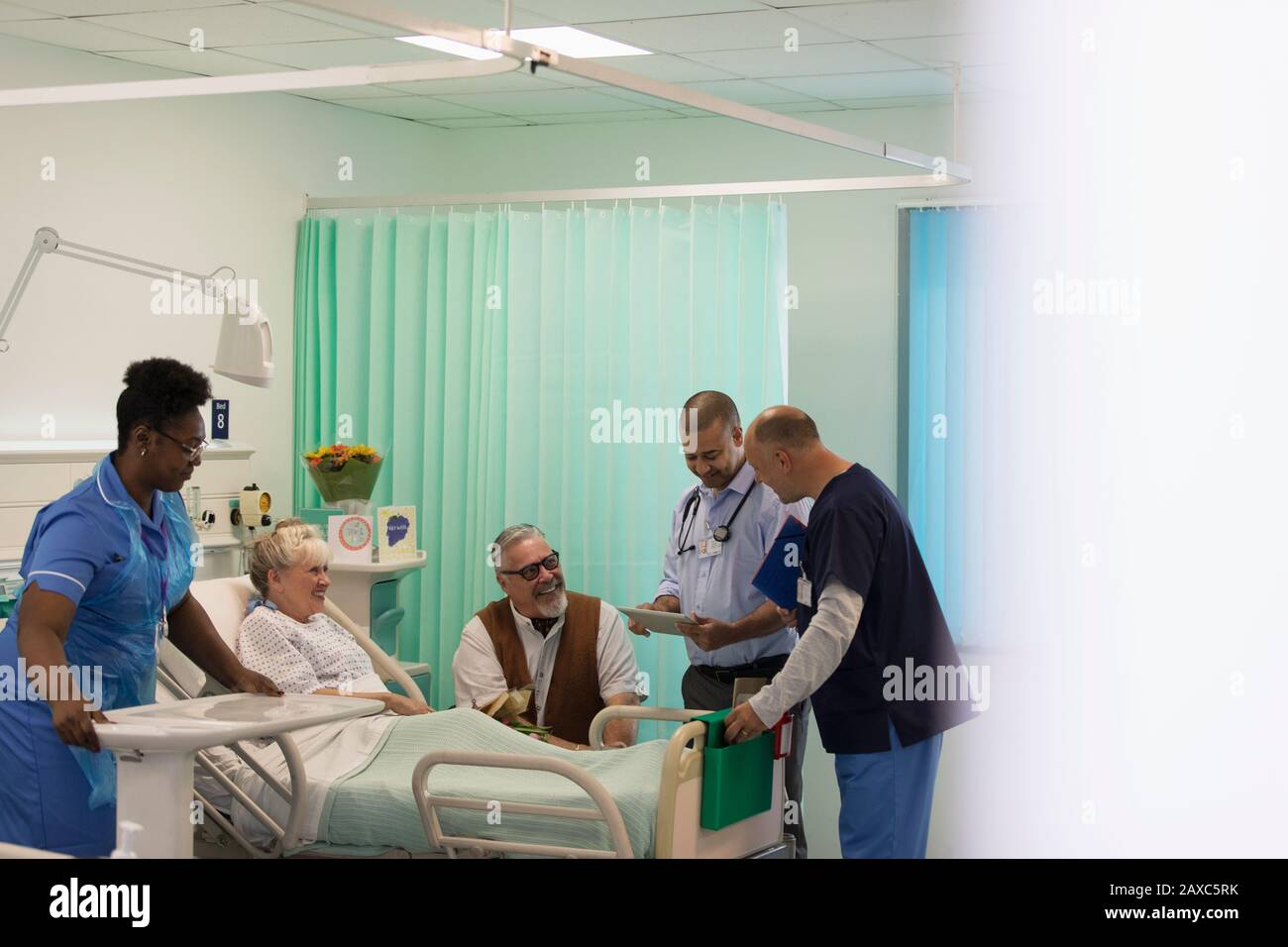 Ärzte machen Runden und sprechen mit dem leitenden Patienten im Krankenhauszimmer Stockfoto