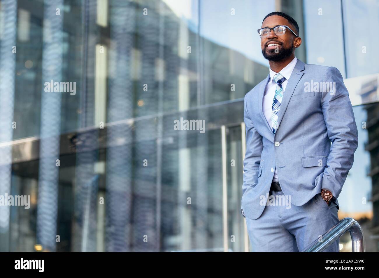 Junger, versierter unternehmer des afroamerikanischen CEO, stilvoller Anzug und Brille, die selbstbewusst im Bürogebäude des Arbeitsplatzes stehen Stockfoto