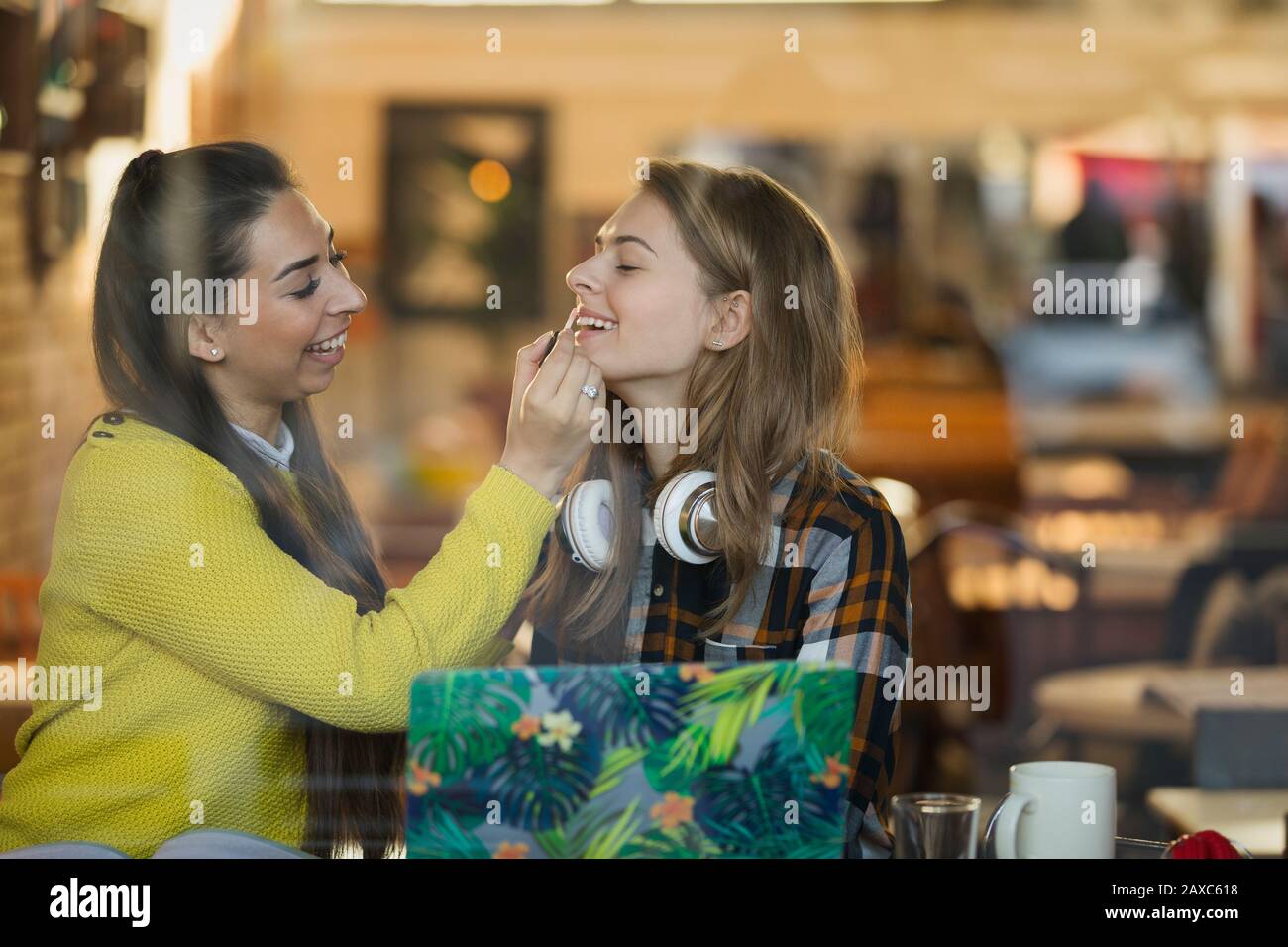 Junge Frau, die Lippenglanz auf die Lippen der Freunde im Café-Fenster anwendet Stockfoto