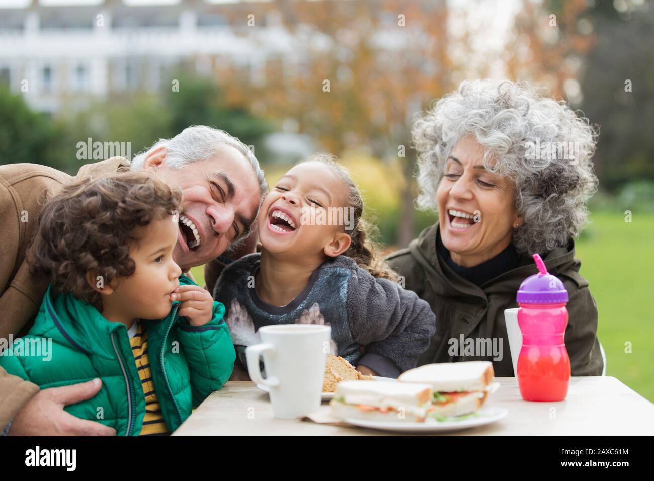 Verspielte Großeltern und Enkel lachen und essen im Park zu Mittag Stockfoto
