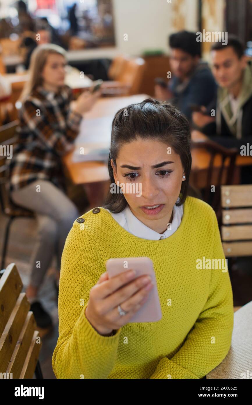Besorgte junge Frau mit Smartphone im Café Stockfoto