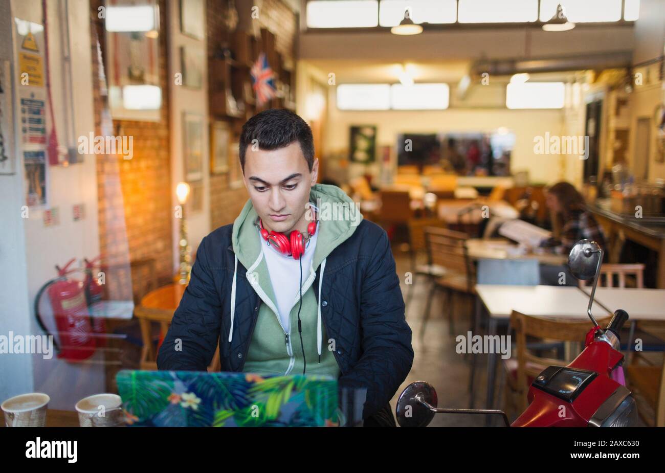 Konzentrierter junger Student der männlichen Hochschule, der am Laptop im Café-Fenster studiert Stockfoto