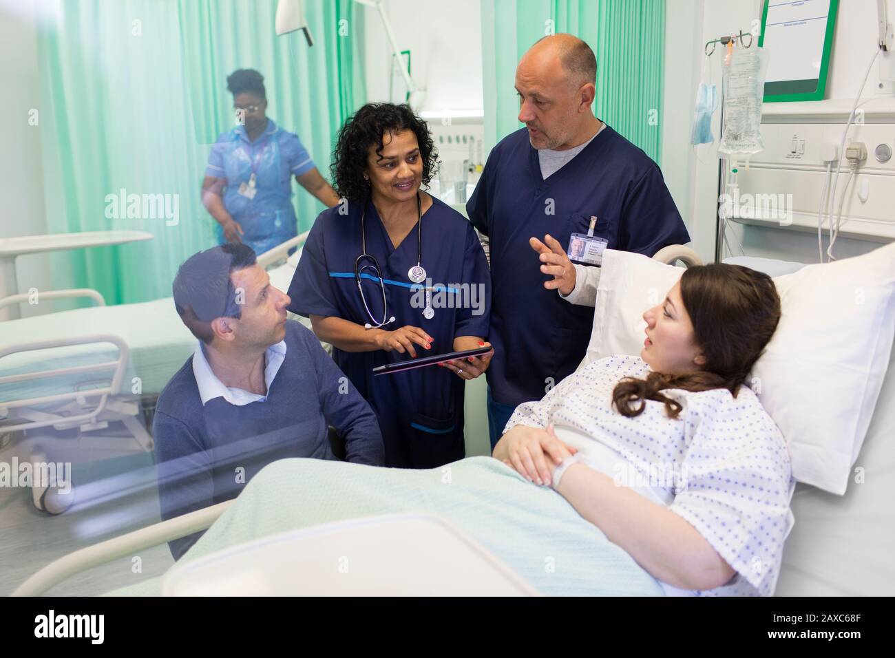 Ärzte mit digitalen Tabletts machen Runden und sprechen mit Paaren in der Krankenstation Stockfoto