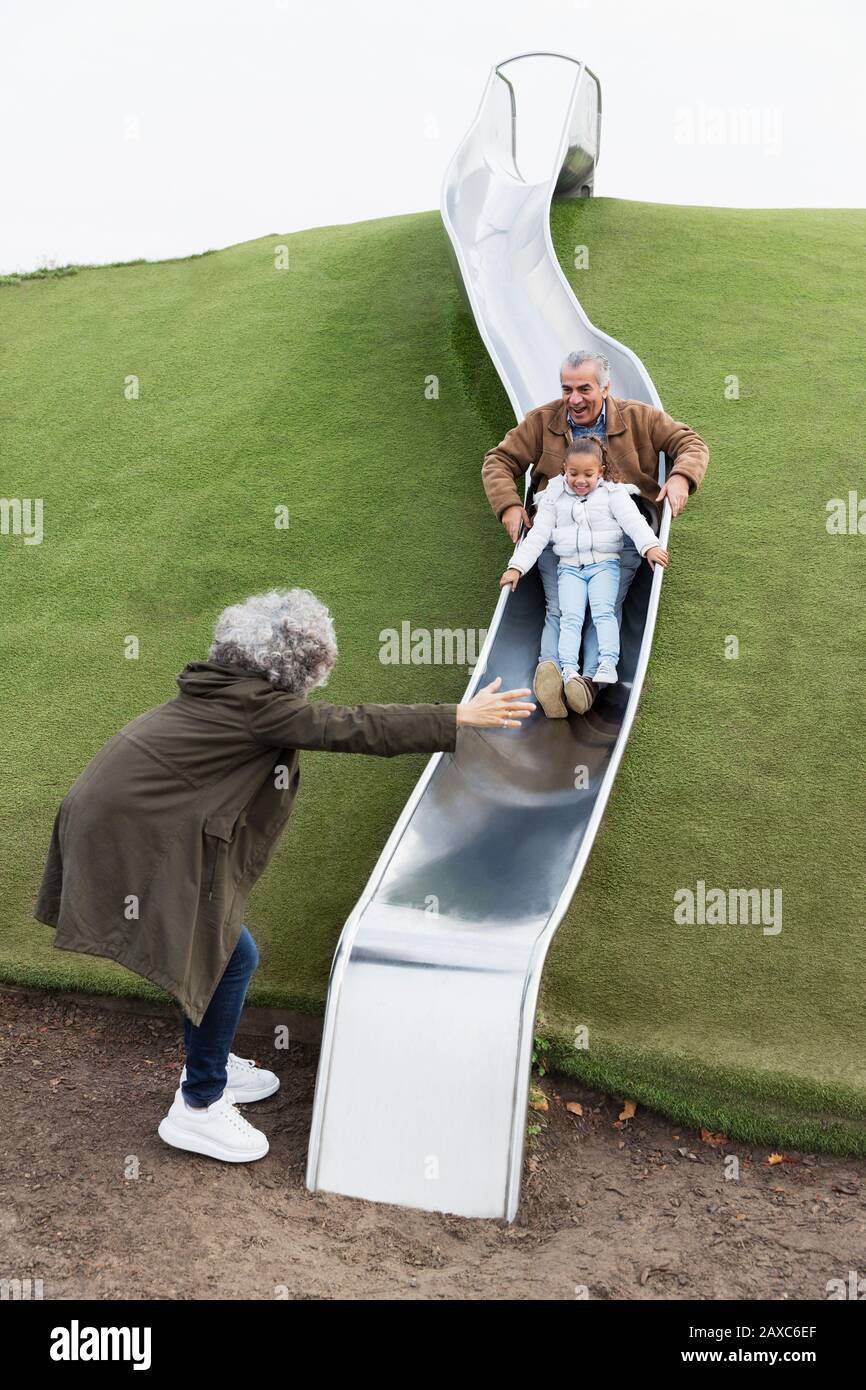 Großeltern mit Enkelin auf Spielplatzrutsche Stockfoto