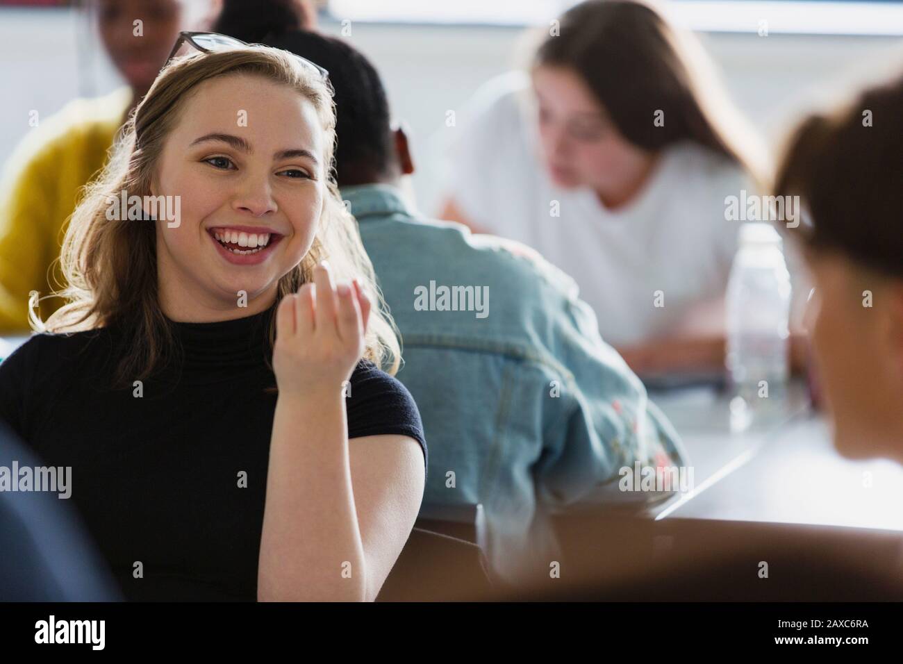 Fröhliche, lächelnde Schülerin der High School, die mit Klassenkameradin im Klassenzimmer spricht Stockfoto