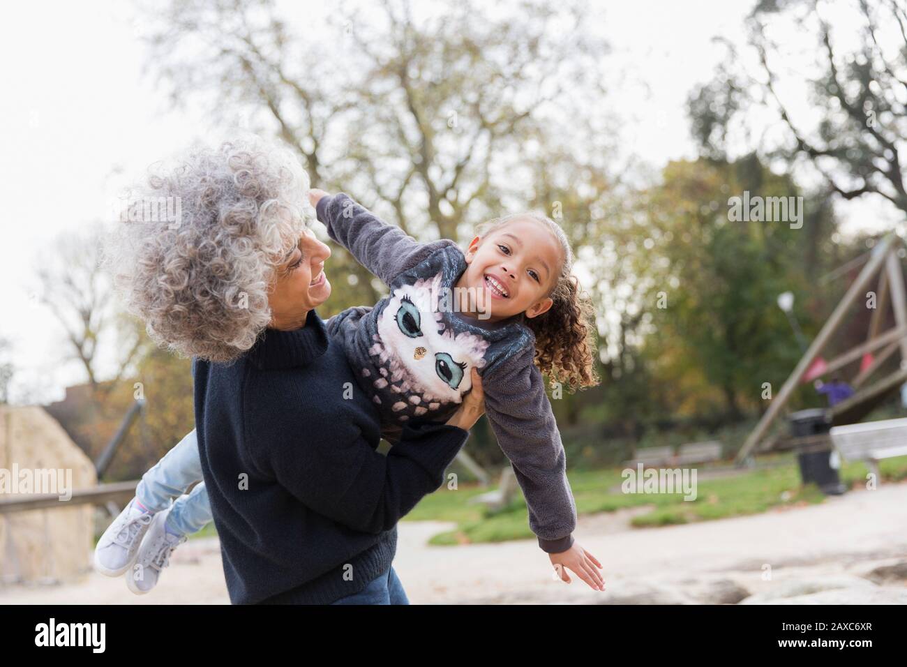 Portrait verspielte Großmutter hebt Enkelin auf dem Spielplatz Stockfoto