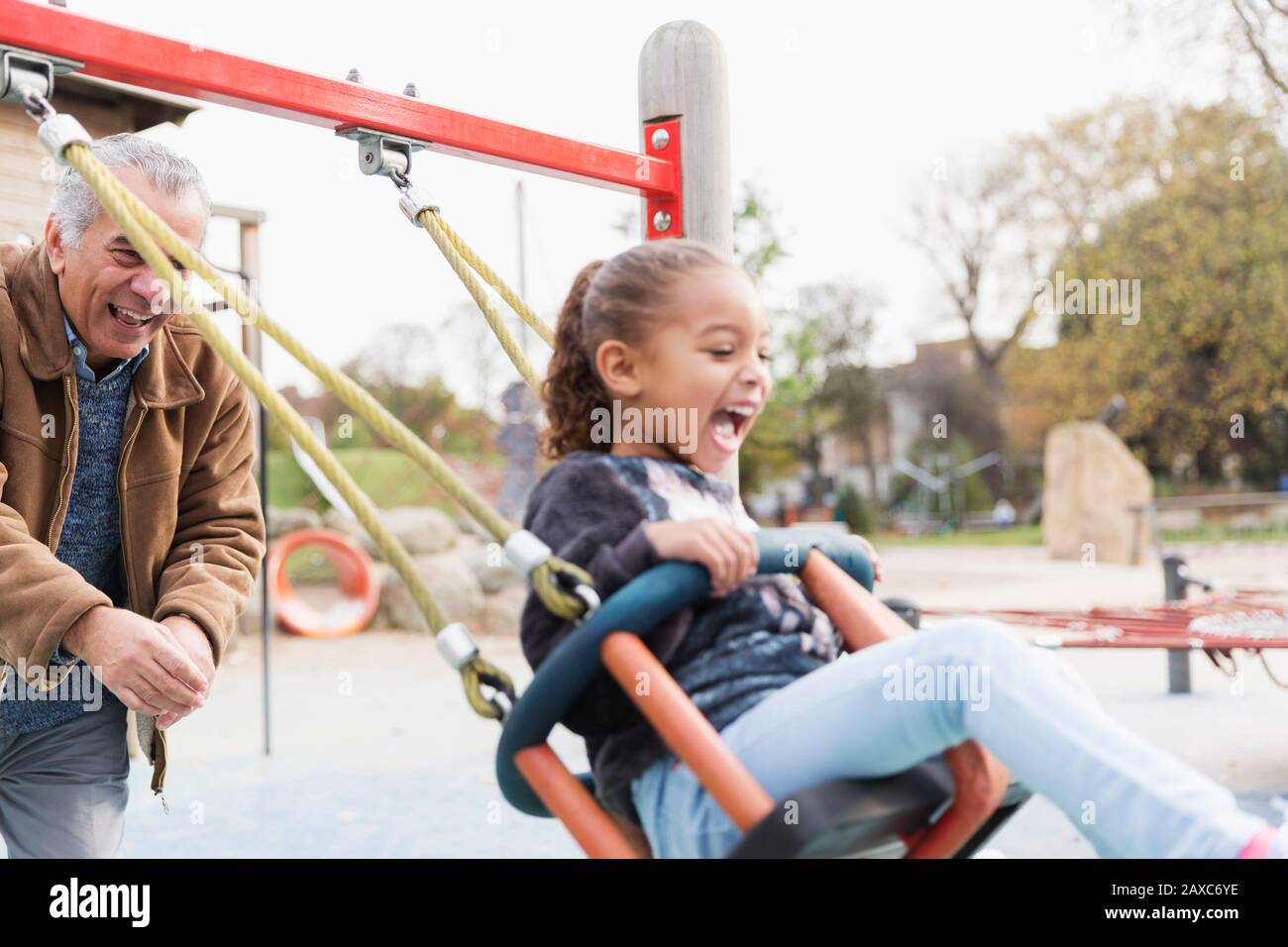 Verspielter Großvater treibt Enkelin auf Spielplatzschwinge Stockfoto