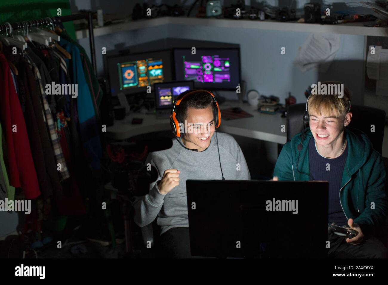 Aufgeregte Teenager mit Kopfhörern, die Videospiele am Computer im dunklen Raum abspielen Stockfoto