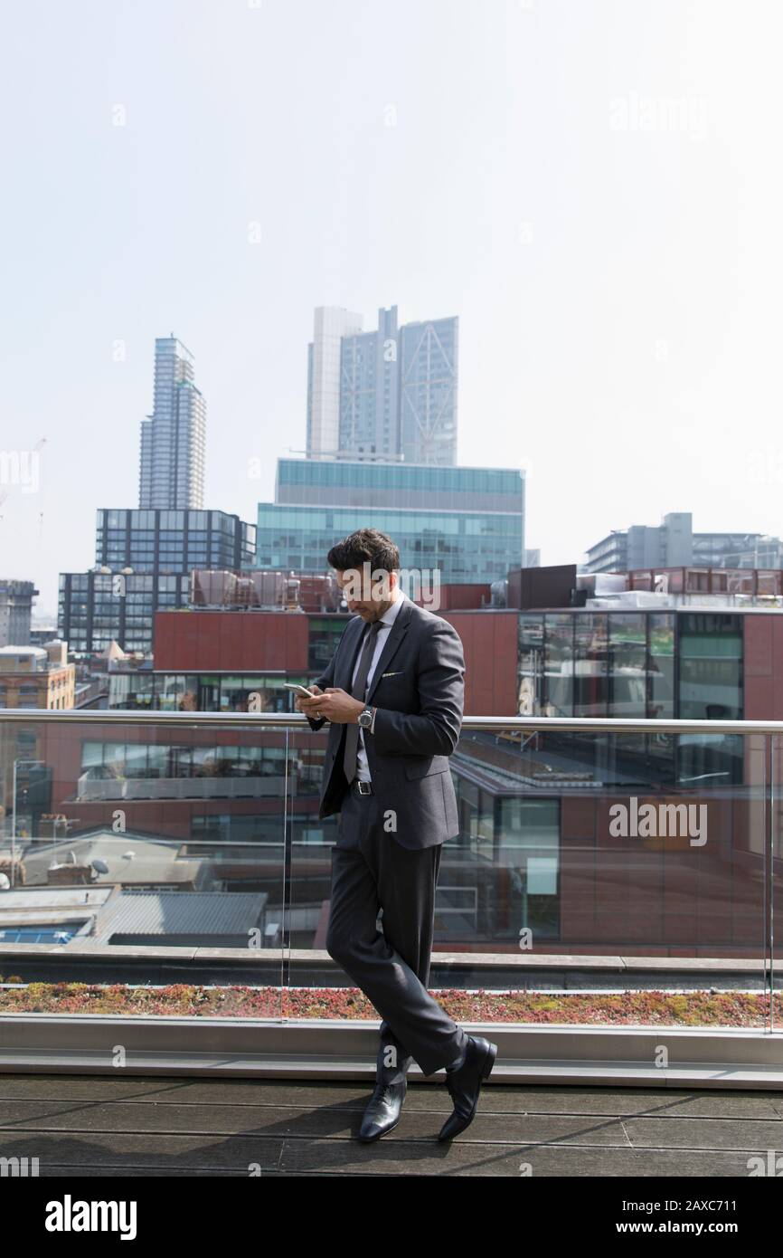 Geschäftsleute nutzen Smartphone auf dem sonnigen, städtischen Hochhausbalkon Stockfoto